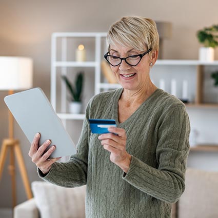Mature woman paying with debit card while using tablet